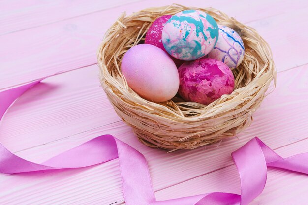 Colorful easter eggs in a nest on pink wooden table