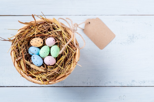 Foto uova di pasqua variopinte in nido di paglia con l'etichetta su fondo di legno blu