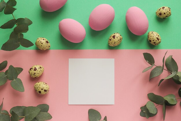 Colorful easter eggs and quail eggs on geometric pink and green table with empty paper blank