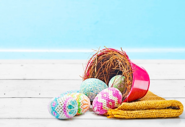 Colorful easter eggs spilled from the nest in a red bucket with fabric on a wooden table. Happy Easter