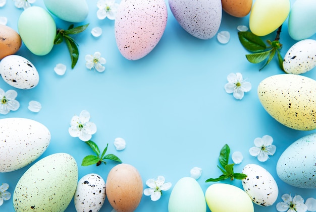 Colorful Easter eggs with spring blossom flowers over blue background.