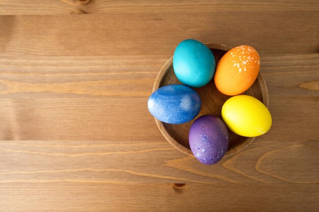 Colorful easter eggs in a wooden bowl on a wooden background