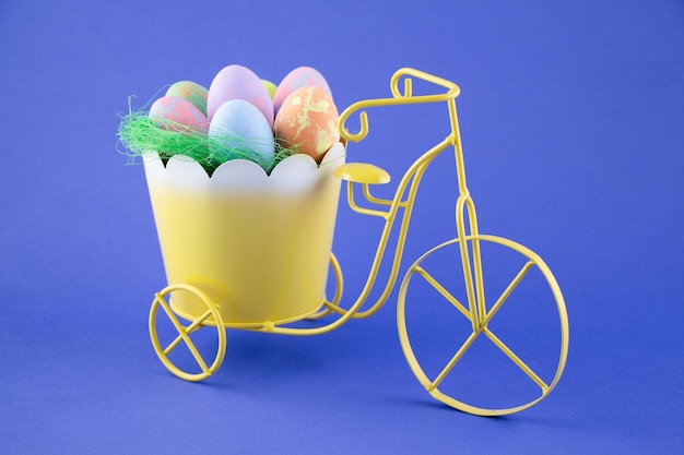青い背景の黄色い自転車のバスケットにカラフルなイースターエッグ自転車はイースターを急いでいます