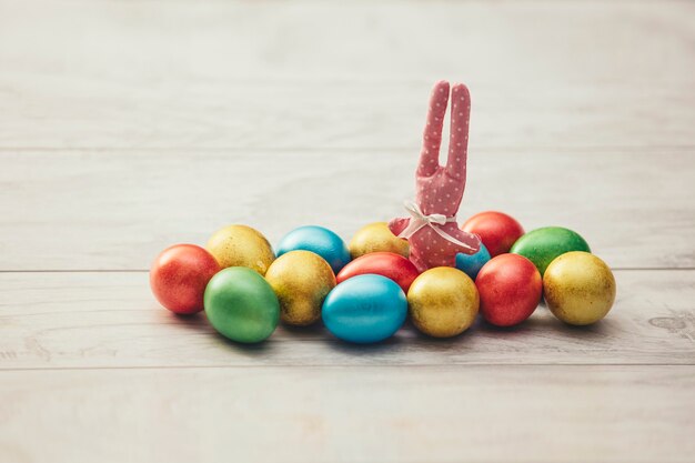 다채로운 부활절 휴일 달걀은 나무 테이블에 반짝이며 장난감 토끼입니다.