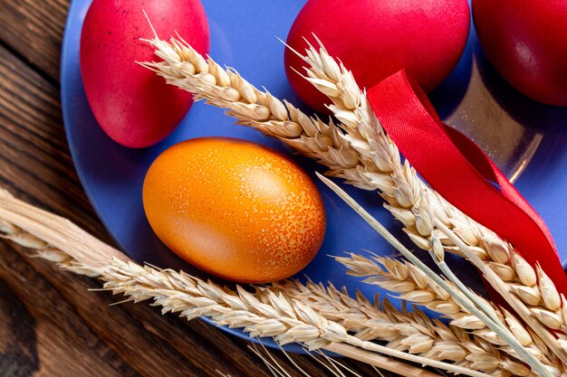 Colorful eggs for Easter on blue plate with ears of grain, on brown wooden 