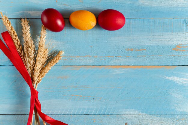 Colorful eggs for Easter with ears of grain on blue wooden background