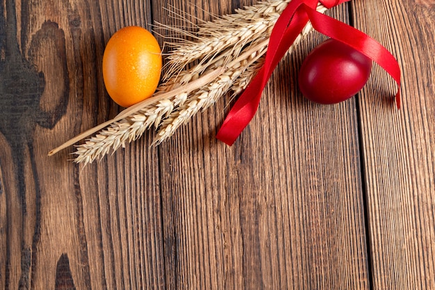 Colorful eggs for Easter with ears of grain on brown wooden  with copy space