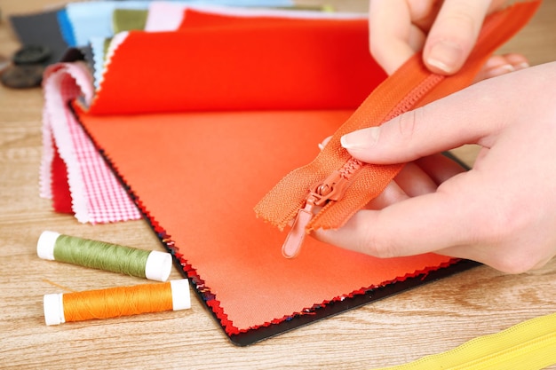 Photo colorful fabric samples and zipper in female hands on wooden table background