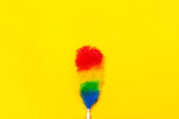 Colorful feather duster on yellow background. cleaning concept