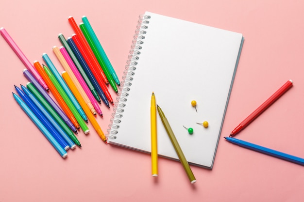 Colorful felt tip pens with blank notepad paper on pink pastel background