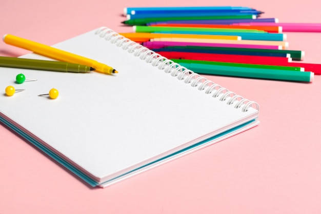 Colorful felt tip pens with blank notepad paper on pink pastel background