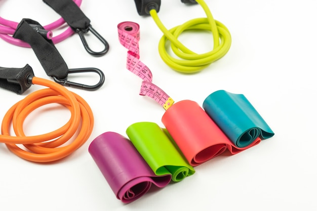 Fasce elastiche colorate per il fitness e espansori, un metro a nastro rosa si trovano su un pavimento bianco