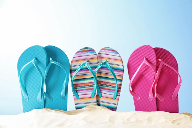 Colorful flipflops on sand against color background Summer vacation concept