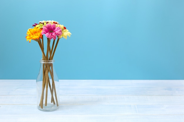 Photo colorful flowers in clear bottle on light blue table in front of blue wall.