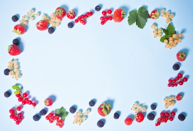 Colorful frame made with blackberry, strawberry, red and white currant on blue