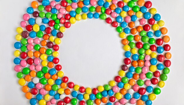 Colorful frame of multicolored candy dragees round bonbons scattered on white background