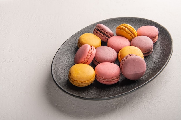 Stack di macaron francese o italiano colorato sul piatto scuro messo sul tavolo bianco con per