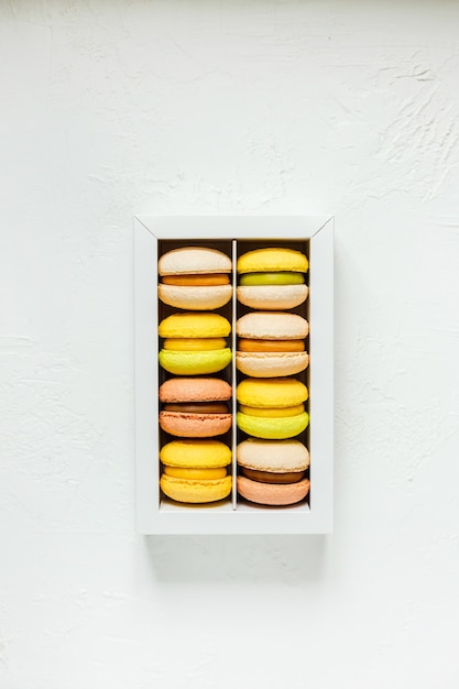 Colorful french macarons in a white box on white, top view