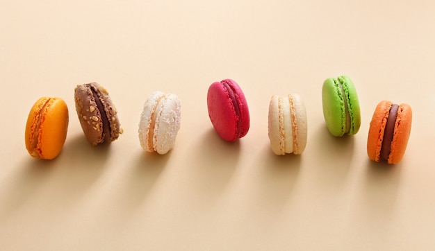 Photo colorful french macaroons on beige background. almond cookies.top view, flat lay. valentine's day sweet gift concept,holiday, celebration.