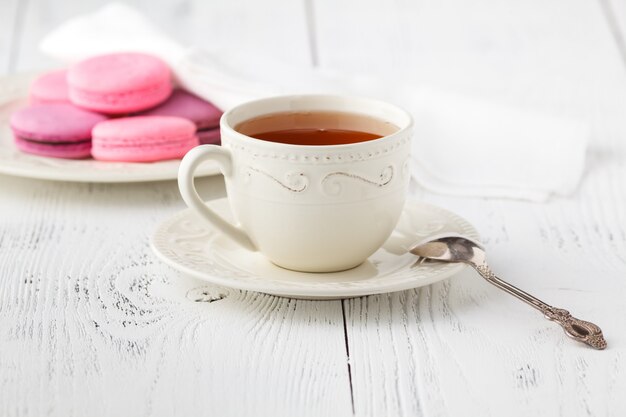 Colorful French macaroons and cup of tea on a rustic wooden surface, selective focus