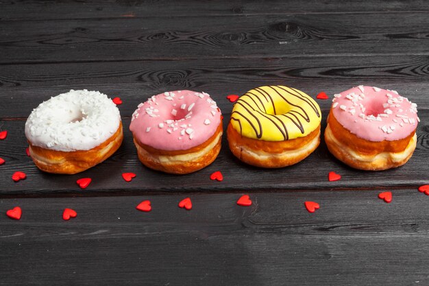 Colorful fresh donuts on dark black wooden surface