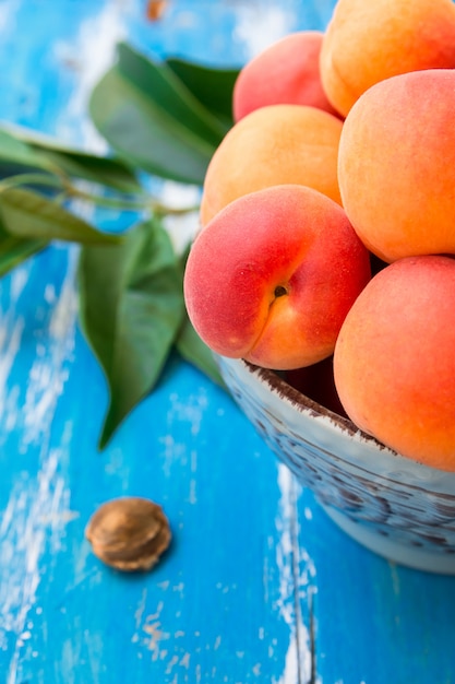 Colorful fresh ripe organic whole apricots in ceramic bowl on blue wood