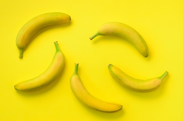 カラフルなフルーツ柄。黄色の背景上のバナナ。上面図。ポップアートデザイン、創造的な夏のコンセプト。最小限の平置きスタイル。