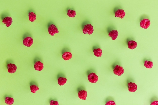 Colorful fruit pattern of wild berries on green background Raspberries Top view Flat layRipe sweet red berries pattern Concept of healthy and dieting eating