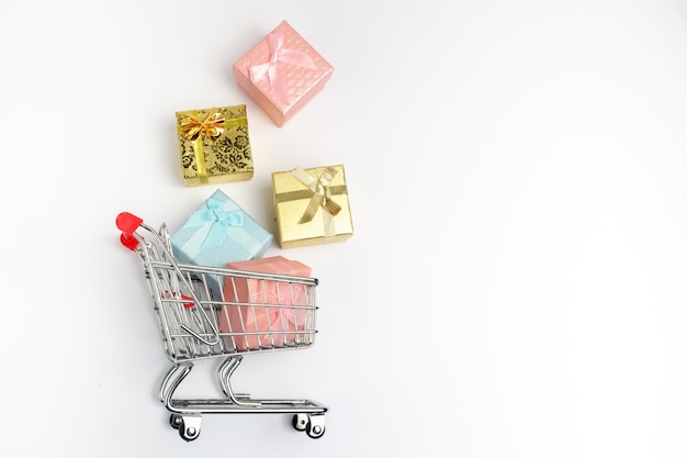 Colorful gifts box, supermarket shopping cart on white wooden background