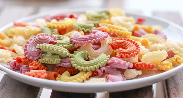 Colorful green, yellow, white, orange and pink italian crown pasta on white plate