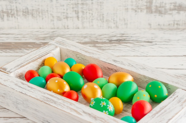 Colorful hand painted easter eggs in white wooden box on wooden table with copy space.