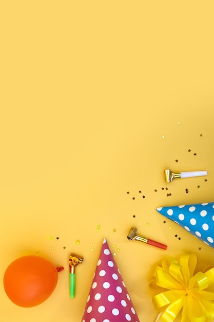 Colorful happy birthday or party background Flat Lay with birthday hats, blowers, confetti and ribbons on yellow background. Top View with Copy space.