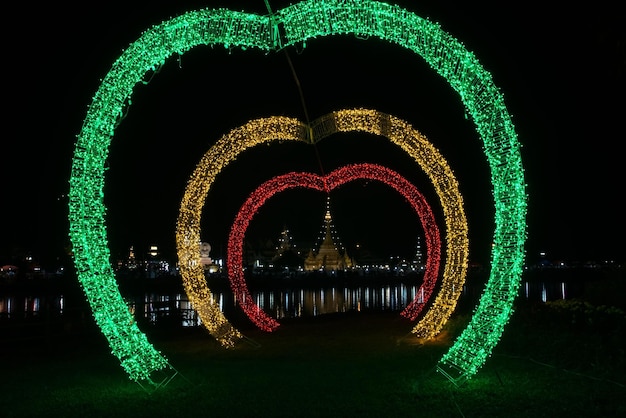 Colorful heart like LED light arch with Buddhist pagoda in background, Thailand