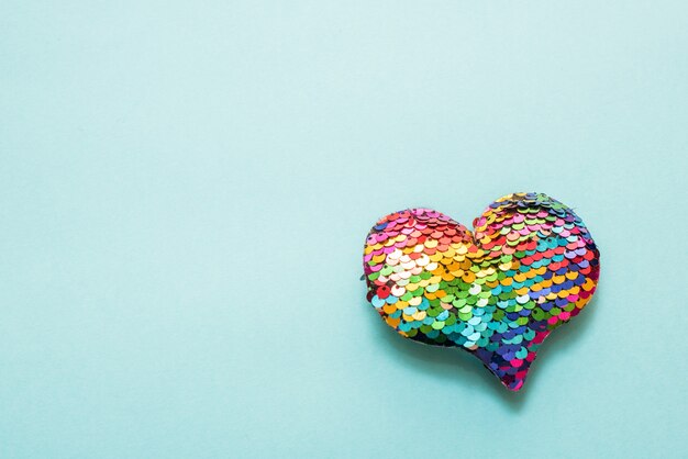 Colorful heart made of sequins on a turquoise wall. Copy space