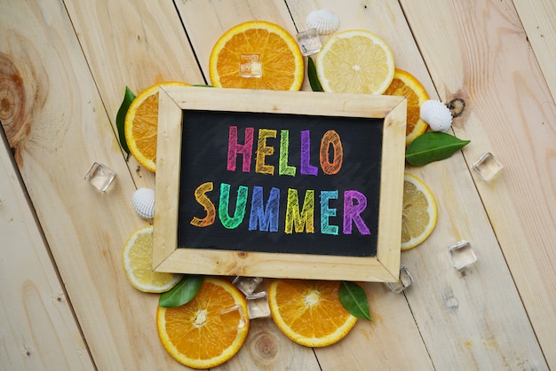 Photo colorful hello summer text on blackboard orange leaves cube ice sea shells citrus