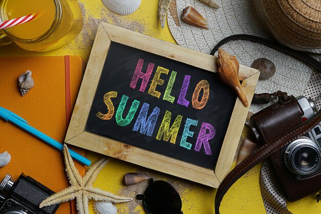 colorful hello summer text on blackboard between summer beach accessories 