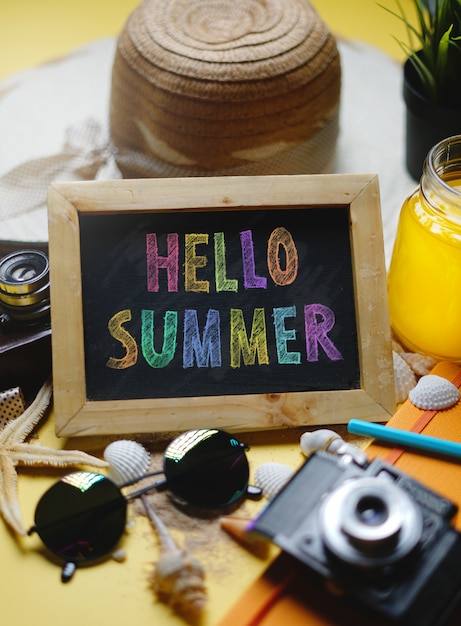 colorful hello summer text on blackboard between summer beach accessories 