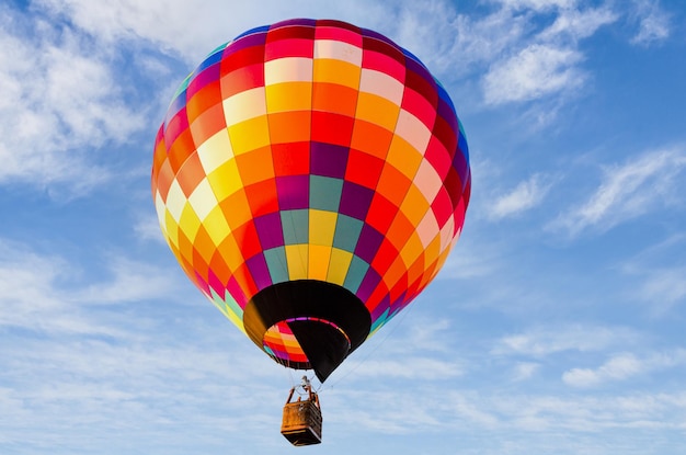 Colorful hot air balloon flying over blue sky with white clouds.