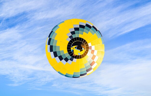 Colorful hot air balloon flying over blue sky with white clouds.