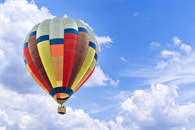 Colorful hot air balloon flying over blue sky with white clouds