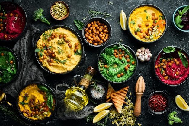 Colorful hummus bowls green yellow and beetroot hummus on dark background with lemon olive oil and spices On a concrete black background