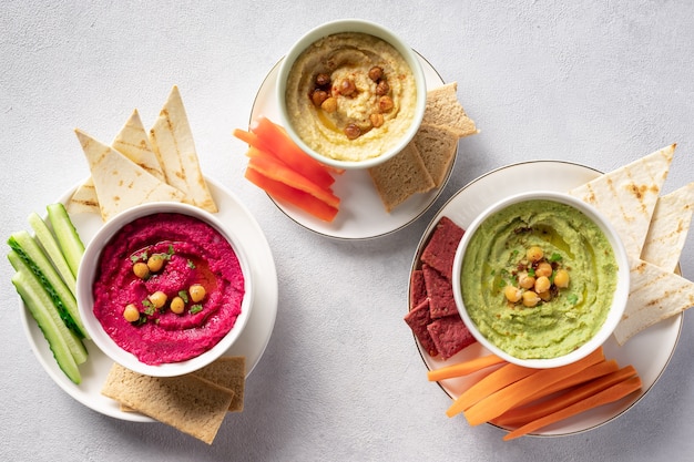 Colorful hummus in bowls, served with vegetables sticks