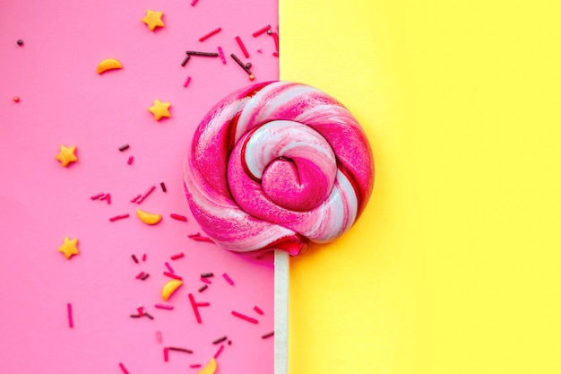 Colorful lollipop with sugar topping isolated over pink and yellow paper wall. Flat lay. Copy space. Minimal concept