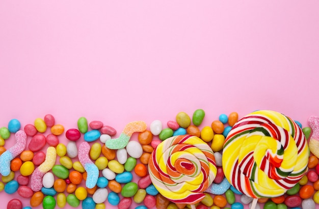 Colorful lollipops and different colored round candy on pink