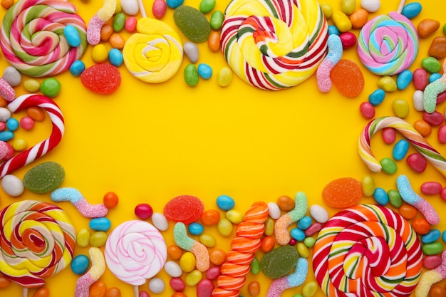 Colorful lollipops and different colored round candy on yellow 