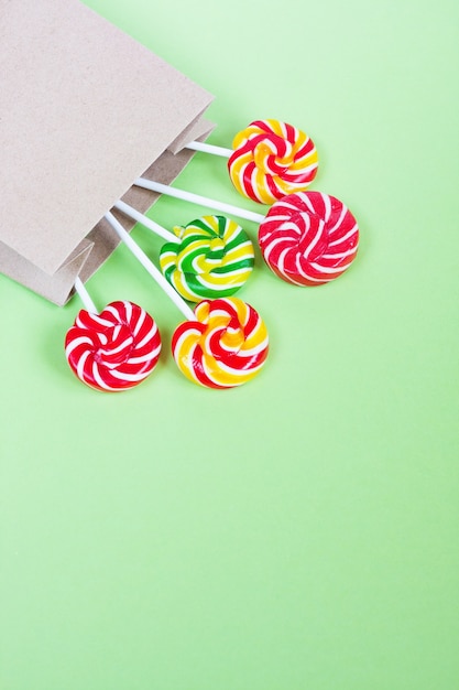 Colorful lollipops in paper bag on green background.