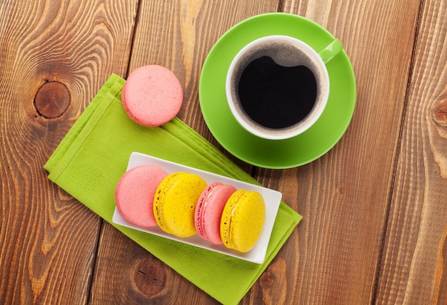 Colorful macaron cookies and cup of coffee on wooden table background