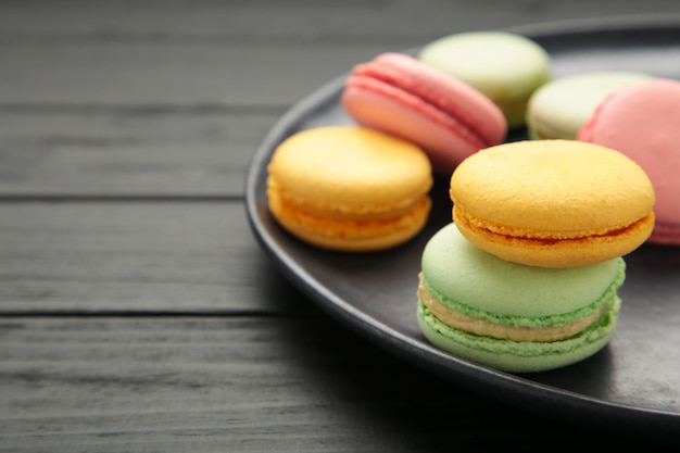 Colorful macarons cakes on black background small french cakes\
on plate space for text