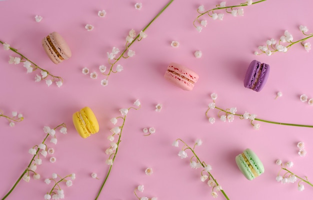 Colorful macarons or macaroons decorated with blooming lily of the valley flowers on pastel pink. Sweet french dessert concept. Flat lay