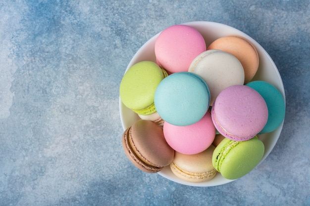 Colorful macarons in a white plate on a blue surface